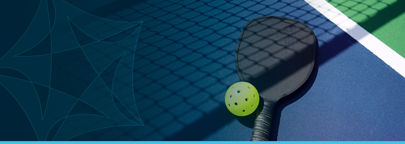 A pickleball racket and ball sit on a court.